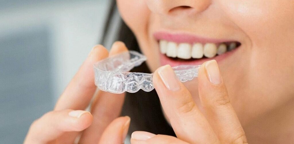 Close-up of a woman holding a clear dental aligner, showcasing dental health and a bright smile.